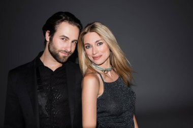 Stylish couple smiling at camera on grey background 