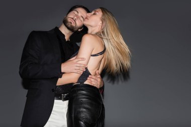 Low angle view of sexy blonde woman hugging bearded man on grey background 