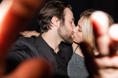 Side view of stylish couple kissing during party on black 