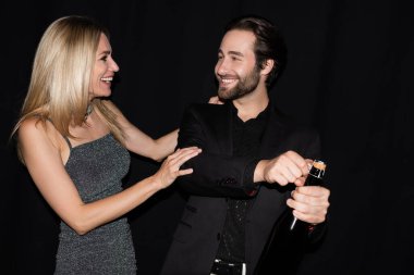 Smiling woman hugging boyfriend with bottle of champagne isolated on black 