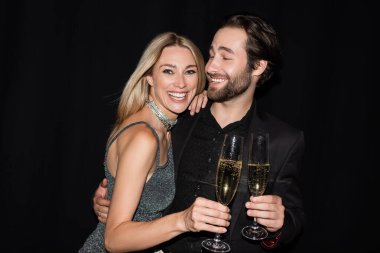 Bearded man hugging cheerful girlfriend with glass of champagne isolated on black 