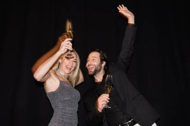 Motion blur of cheerful couple holding champagne during party isolated on black 