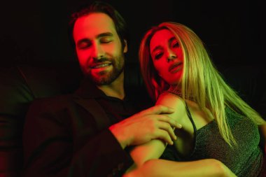Smiling man touching blonde girlfriend in dress with lighting isolated on black 