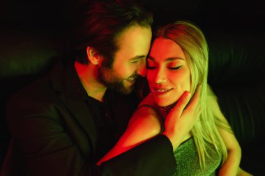 Positive man touching sexy blonde girlfriend with lighting isolated on black 