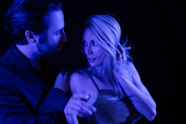 Young man touching blonde girlfriend with blue lighting isolated on black 