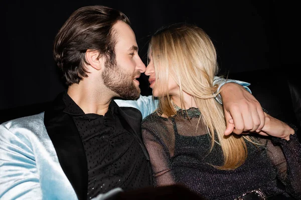 Side view of stylish man kissing blonde girlfriend isolated on black 