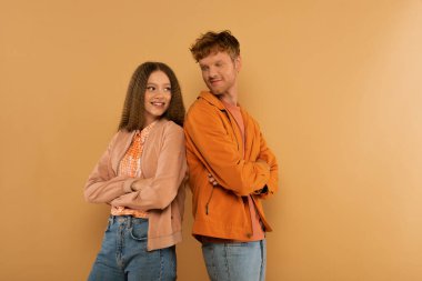 happy young couple in jackets standing with crossed arms isolated on beige 