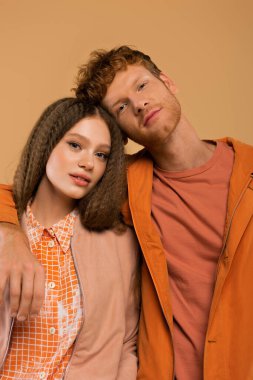 redhead young man in orange jacket hugging girlfriend isolated on beige