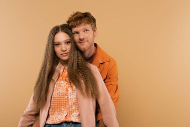 joyful young man with red hair near smiling girlfriend isolated on beige