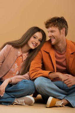 cheerful girl leaning on shoulder of happy boyfriend isolated on beige