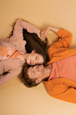 top view of pleased and young redhead man lying together with pretty girlfriend on beige