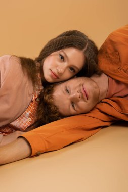 pleased and young redhead man lying together with pretty girlfriend on beige