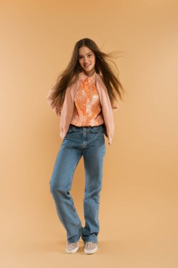 full length of happy teenage girl in autumnal and casual clothes posing on beige