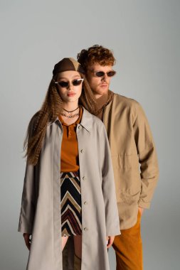 young and stylish couple in autumnal outfits posing isolated on grey