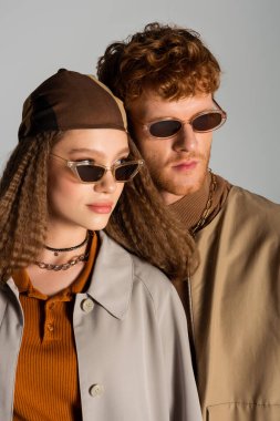 portrait of young stylish couple in autumnal outfits and sunglasses posing isolated on grey