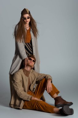 full length of teenage girl in trench coat standing near stylish boyfriend on grey