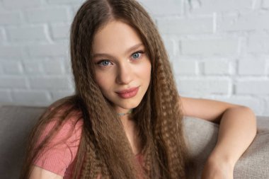 portrait of pretty teenage girl in casual clothes sitting on couch in modern living room 