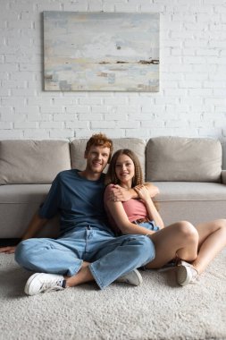 redhead and happy young man hugging pretty girlfriend in living room 