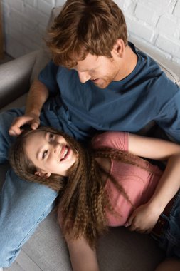 top view of redhead and smiling young man stroking hair of cheerful girlfriend in living room 