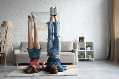 young couple doing shoulder stand exercising in modern living room