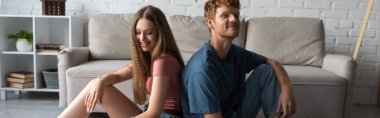 happy young couple sitting next to each other in modern living room, banner