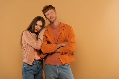 redhead young man standing with crossed arms near girl isolated on beige
