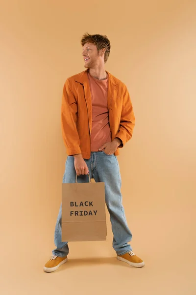 Positive Young Man Red Hair Holding Shopping Bag Black Friday — Φωτογραφία Αρχείου
