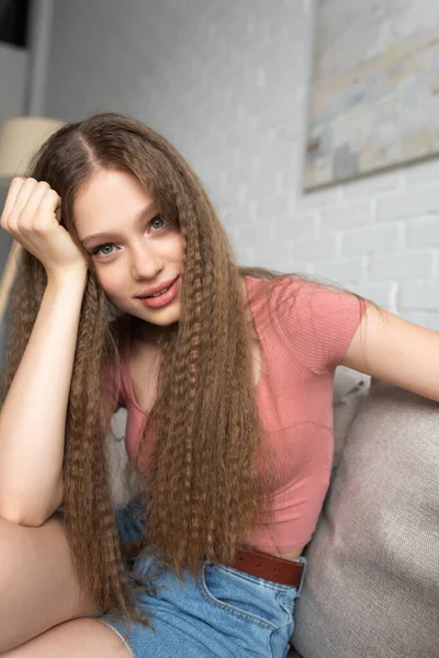 smiling teenage girl in casual clothes sitting on couch in modern living room 