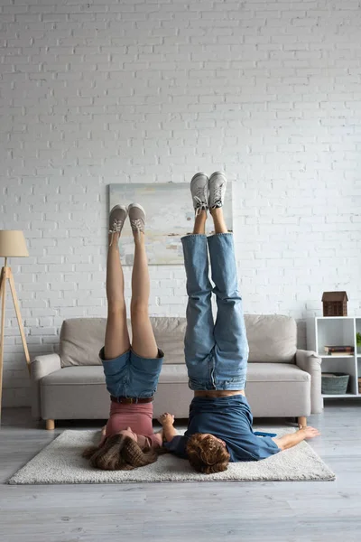 young couple doing shoulder stand exercising near couch in modern living room