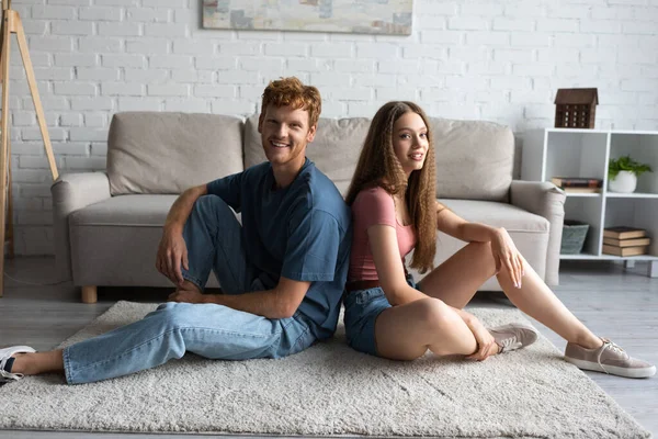 Full Length Happy Young Couple Sitting Carpet Looking Camera Living — Foto Stock