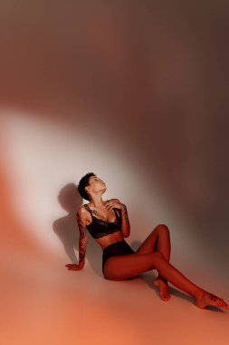 İnce ve seksi vücutlu, kırmızı arka planda siyah iç çamaşırlı, gölgeli bir kadın.