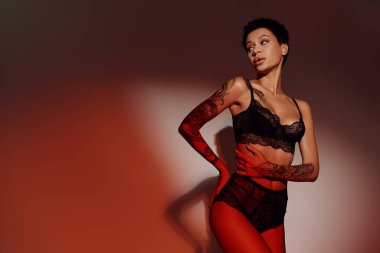 Siyah dantelli iç çamaşırlı seksi kadın elleri kalçasında kırmızı ve kahverengi arka planda poz veriyor.