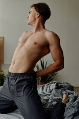 sexy shirtless man in pajama pants stretching back while kneeling on bed clipart