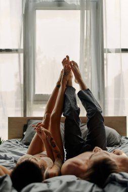 Genç çift yatakta uzanırken el ele tutuşup birbirlerine dokunuyorlar. 