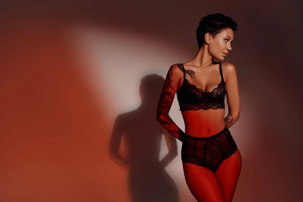 魅力的でスレンダーな女性で黒ランジェリー姿で手後ろに赤と茶色の背景 — ストック写真