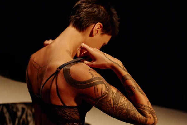 黑发纹身女人坐在米色和黑色背景下脱下胸罩的背影 — 图库照片
