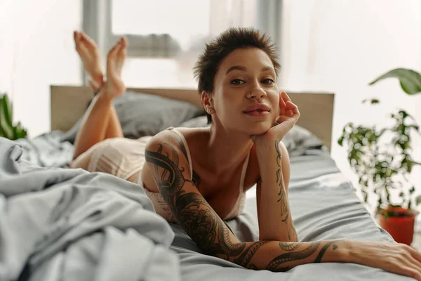 Getatoeëerde Vrouw Lingerie Kijken Naar Camera Terwijl Liggend Grijs Beddengoed — Stockfoto