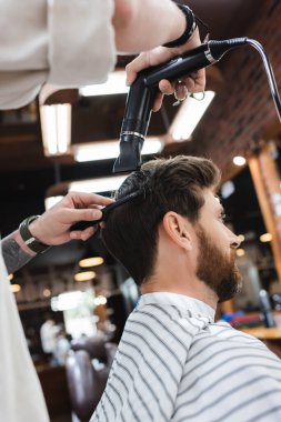 Kuaförün düşük açılı görüntüsü berber dükkanında esmer adamın saçlarını kurutuyor.
