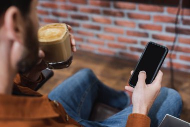 Bir bardak cappuccino ile bulanık adam kısmi görüntüsü boş ekran ile akıllı telefon tutan
