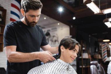 Kuaför pelerinli esmer genç berbere yakın gülümsüyor güzellik salonunda boynunu kesiyor.
