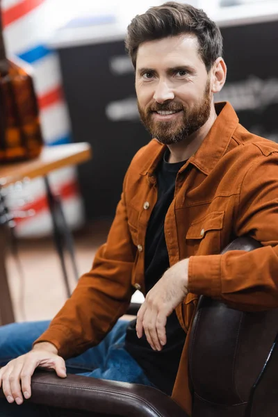 Bearded Man Smiling Camera While Sitting Blurred Barbershop — Stock Photo, Image