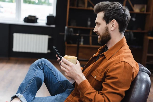 Vista Lateral Del Hombre Sonriente Con Cappuccino Utilizando Teléfono Móvil —  Fotos de Stock