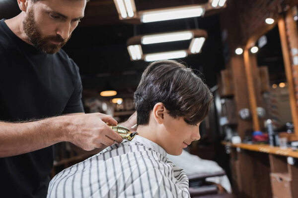 brunette teenage boy in hairdressing cape near bearded barber trimming his neck 