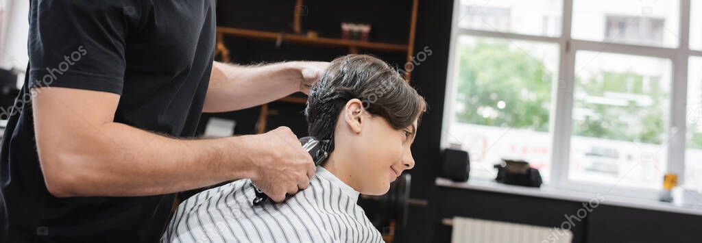 side view of hairdresser trimming neck of teenage client in barbershop, banner
