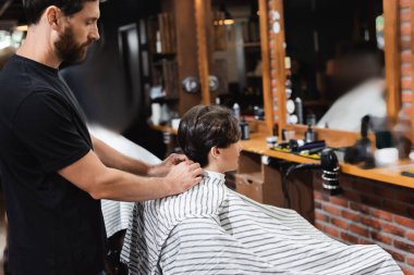 Güzellik salonunda genç bir çocuğa pelerin takan bir kuaför. 