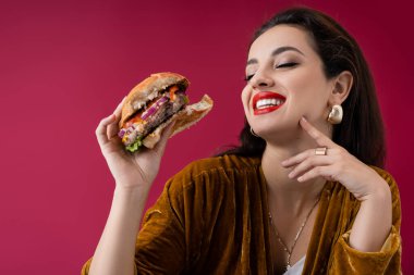 Mutlu ve modaya uygun esmer kadın kırmızı üzerine izole edilmiş lezzetli bir burger tutuyor.
