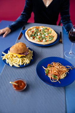 Kızarmış patates kızartması, pizza ve makarna ile hamburgerin yanındaki bulanık kadın görüntüsü