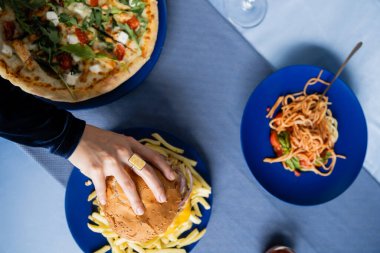 Makarna ve pizzalı patates kızartması ve tabağın yanında hamburger yiyen bir kadının en iyi görüntüsü.