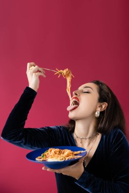 Kadife elbiseli esmer kadın kırmızı tabaktaki lezzetli spagettiyi yiyor. 
