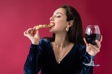 Kırmızıda izole edilmiş İtalyan pizzası yiyen zarif esmer kadın.